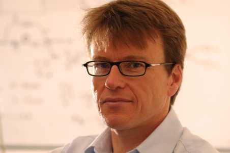 A middle-aged man with short brown hair and glasses looks directly at the camera in a professional setting.